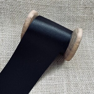 Pu&ograve; includere: Un rotolo di nastro di raso nero avvolto attorno a un rocchetto di legno.