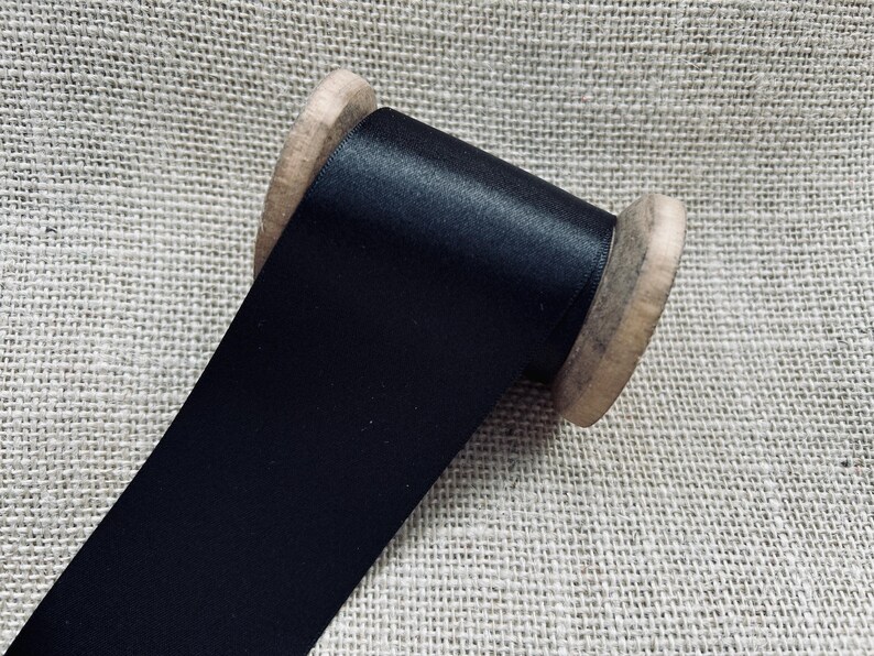 Pu&ograve; includere: Un rotolo di nastro di raso nero avvolto attorno a un rocchetto di legno.