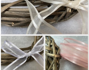 May include: Three different colors of sheer ribbon tied around a woven heart-shaped wreath. The ribbons are white, ivory, and pink.