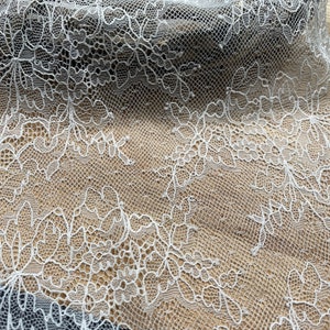 May include: White lace fabric with a delicate floral pattern. The lace is sheer and has a soft, flowing texture.