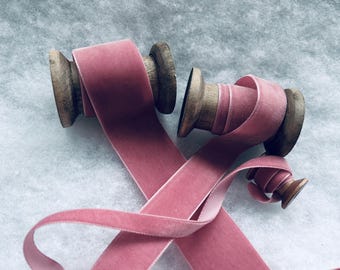 May include: Two spools of dusty rose pink velvet ribbon, each wound around a wooden spool. The ribbon is soft and luxurious, perfect for adding a touch of elegance to any project.