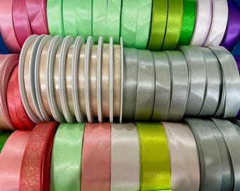 May include: Assortment of colorful satin ribbon spools in various widths. The ribbons are arranged in rows, with each row featuring a different color. The colors include pink, green, beige, silver, and white.