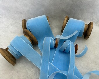 May include: Four spools of light blue velvet ribbon. The ribbon is wound around wooden spools.