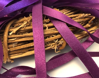May include: Purple satin ribbon spools arranged in a criss-cross pattern on a white background. The ribbon is a deep purple color and has a subtle sheen.