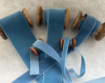 May include: Four spools of blue velvet ribbon, each wound around a wooden spool. The ribbon is a light blue color and has a subtle sheen.