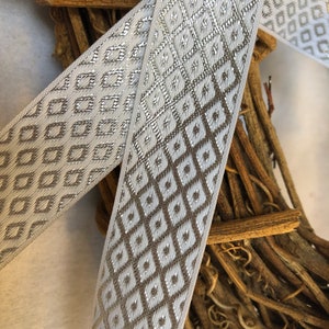May include: White ribbon with a silver geometric pattern. The ribbon is woven with a diamond pattern and has a subtle shimmer.