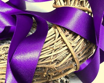 May include: Purple satin ribbon wrapped around a natural woven wreath. The ribbon is shiny and has a smooth texture.