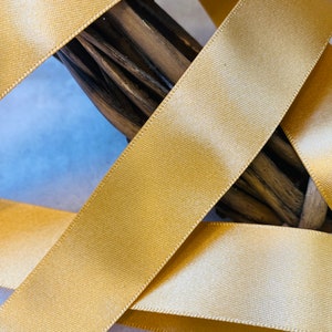 May include: Close-up of gold satin ribbon, showing the texture and sheen of the fabric. The ribbon is folded and layered, creating a decorative effect.