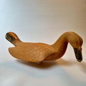 May include: A wooden duck sculpture with a gold-painted beak and wing tips. The duck is carved with detailed feathers and has a natural wood finish.