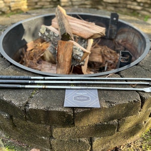 May include: Three silver roasting sticks with forks on the ends, laying on a stone fire pit. A small card with the text "Thank You Old Golf Club" is in the foreground.