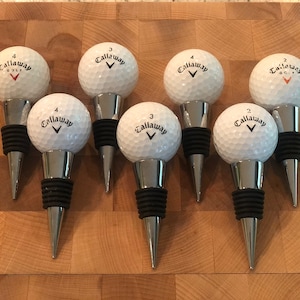 May include: Six silver bottle stoppers with black rubber tops. Each stopper is topped with a white golf ball with the Callaway logo and a number.