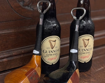 Puede incluir: Dos botellas de vidrio marrón de cerveza Guinness Extra Stout con abridores de botellas de palo de golf negro. Los abridores de botellas están hechos de madera y tienen un acabado negro.