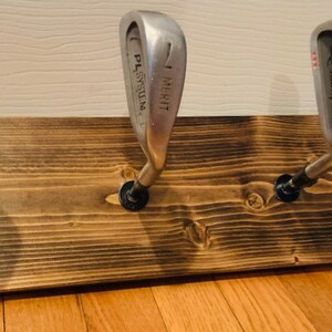May include: A wooden rack with four golf club heads mounted as hooks. The clubs are numbered 6, 7, 4, and 4. The rack is stained a dark brown color.