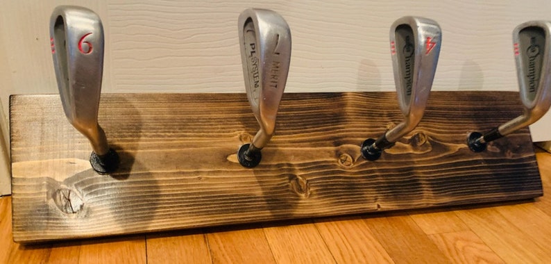 May include: A wooden rack with four golf club heads mounted as hooks. The clubs are numbered 6, 7, 4, and 4. The rack is stained a dark brown color.