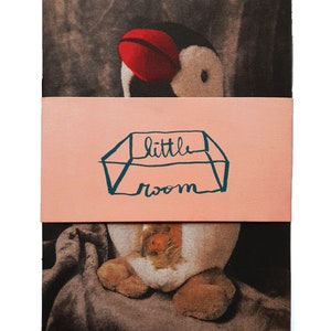 May include: A brown and white stuffed penguin with a red beak and a pink band around its body. The band has the text "little room" written on it.