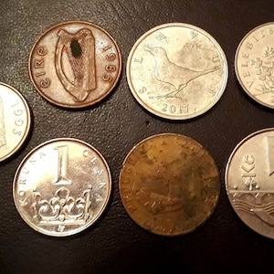 May include: A collection of nine coins from different countries, including Ireland, Czech Republic, and Lithuania. The coins are silver, copper, and gold in color and feature various designs, including a harp, a bird, and a floral pattern.