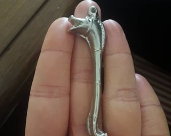 Puede incluir: Un colgante de metal plateado con forma de cabeza de lobo con la boca abierta y un cuerpo largo y delgado.