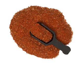 May include: A mound of finely ground, deep reddish-brown spice blend with visible small flecks of dried herbs and seasonings. A small, matte black plastic scoop is partially buried in the center of the spice pile, holding a portion of the mixture.