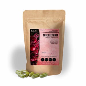 May include: A brown paper bag of "True Beet Root" dietary supplement capsules with a pink label and a picture of beets. Several green capsules are scattered in front of the bag. The label states the supplement is for lower pressure, transport oxygen, main blood sugar, and increase energy.
