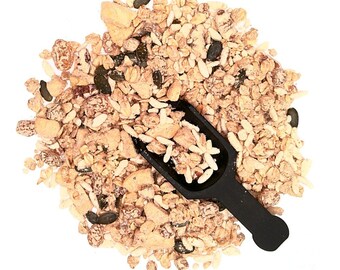 May include: A close-up of a pile of granola with a black scoop. The granola is a mixture of oats, nuts, seeds, and dried fruit.