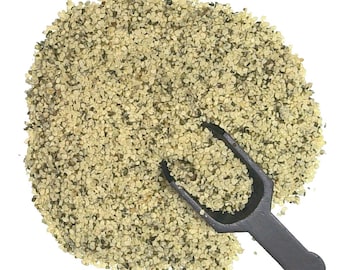 May include: A close-up of a pile of hemp seeds with a small black scoop. The seeds are a light green and tan color.