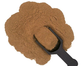 May include: A brown powder, likely ground cinnamon, is piled on a white surface. A black plastic scoop is partially filled with the powder and rests on top of the pile.