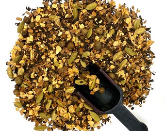 May include: A close-up of a brown wooden scoop filled with a blend of loose leaf tea. The tea blend includes black tea, ginger, cardamom, and other spices.