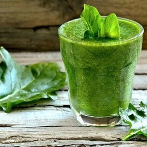 May include: A glass of green smoothie with spinach leaves on a wooden surface.