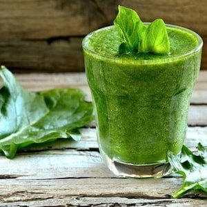 Puede incluir: Un vaso de batido verde con hojas de espinacas sobre una superficie de madera.