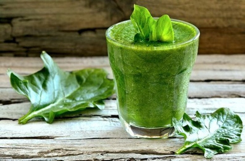 Puede incluir: Un vaso de batido verde con hojas de espinacas sobre una superficie de madera.