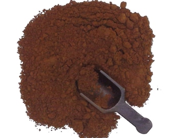 May include: A close-up of a pile of dark brown powder with a small metal scoop. The powder is likely a spice or seasoning.