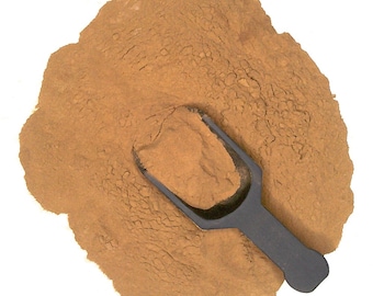 May include: A brown powder with a black scoop. The powder is in a pile on a white surface.