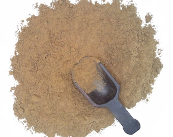 May include: A brown powder with a small black scoop. The powder is spread out on a white background.