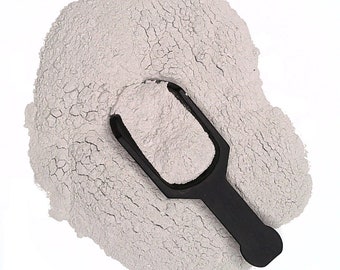 May include: A close-up of a pile of light gray powder with a black plastic scoop. The powder is fine and has a slightly grainy texture.