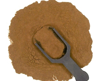 May include: A brown powder with a small black scoop. The powder is spread out on a white background.