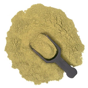 May include: A scoop of green powder sits on a white surface. The powder is a light green color and has a slightly grainy texture. A black plastic scoop is partially buried in the powder.