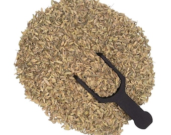 May include: A circular pile of dried, light brown fennel seeds with a small, black plastic scoop resting in the center. The seeds are elongated, textured, and oval-shaped, forming a dense mound against a plain white background.