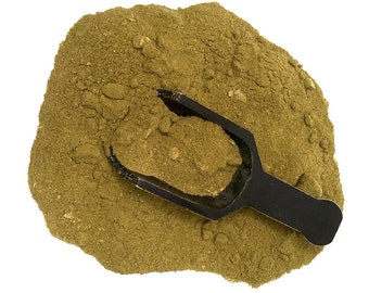 May include: A mound of fine, olive-green herbal powder with a coarse texture. A small, black plastic scoop is partially buried in the center of the powder, filled with a portion of the same green substance, resting against the pile of powder.