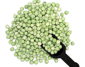 May include: A close-up of a black scoop filled with green dried peas. The peas are scattered around the scoop on a white background.