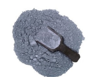 May include: A close-up of a scoop of gray powder, likely cement or plaster, on a white background.