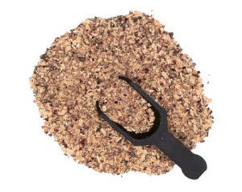 May include: A pile of coarse, light brown and dark brown granular particles with a textured, uneven appearance. A small, solid black plastic scoop with a rounded handle and a wide, open bowl is resting partially submerged in the center of the pile.