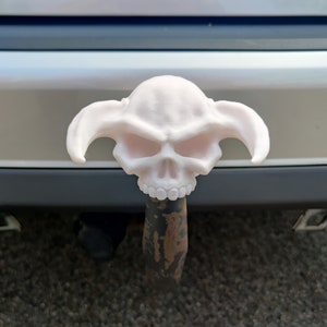 Op de afbeelding: Witte plastic schedel met hoorns, bevestigd aan een trekhaak. De schedel heeft een dreigende uitdrukking met grote oogkassen en een tandenrij.