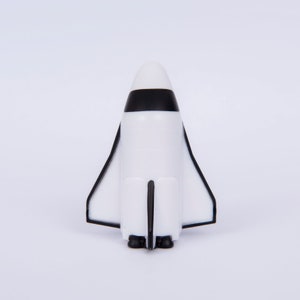 May include: A white and black toy space shuttle with a black stripe around the middle. The shuttle has a black tail fin and two black engines.
