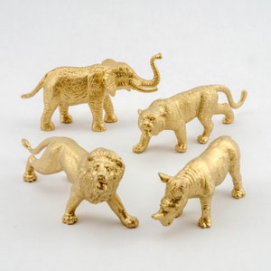 Op de afbeelding: Vier gouden plastic dierenfiguren: een olifant, een tijger, een leeuw en een neushoorn. De figuren zijn op een witte achtergrond gerangschikt.