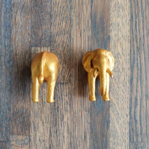 May include: Two gold elephant figurines, one facing forward and the other facing backward. The elephant facing forward has its trunk raised, while the elephant facing backward has its trunk lowered.