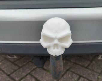 May include: White plastic skull-shaped car hitch cover. The skull has a detailed face with a wide mouth and large eyes.