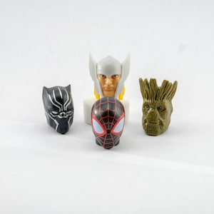 Könnte beinhalten: Vier Superhelden-Figuren: ein schwarzer und silberner Black Panther, ein roter und schwarzer Spider-Man, ein weißer Thor mit einem gelben Umhang und ein grüner Groot.