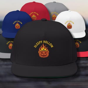 May include: A selection of flat-peak caps in colours such as black, red, blue, and white. Each cap displays the text "Sleepy Hollow" above a jack-o'-lantern design with flames. The caps are presented on a wooden surface.