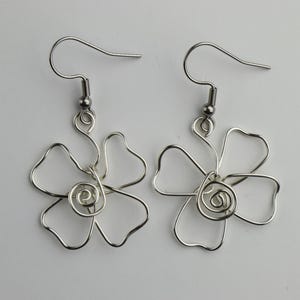 May include: A pair of silver wire earrings shaped like flowers with a spiral in the centre of each flower.