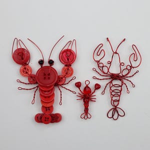May include: Three red lobster sculptures. One lobster is made of red buttons and wire, another is crafted from red wire, and the smallest is made of red beads and wire. The lobsters are displayed on a white background.
